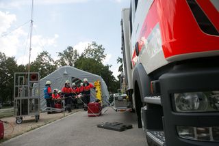 Das Bild zeigt eine Übungssituation. Im Vordergrund steht ein Malteser LKW. Im Hintergrund tragen Einsatzkräfte eine Person aus einem Zelt.