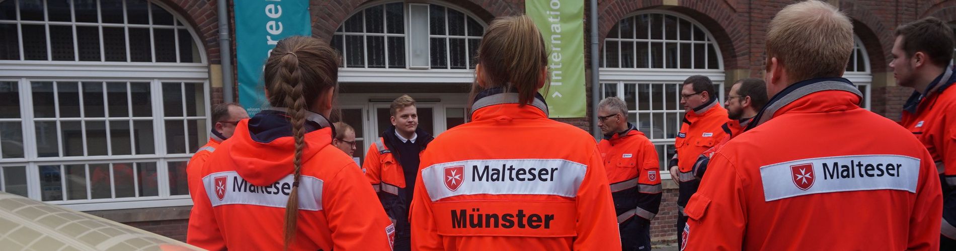 Helferinnen und Helfer stehen zusammen und unterhalten sich. Im Vordergrund ist eine Einsatzjacke mit der Aufschrift Malteser Münster.